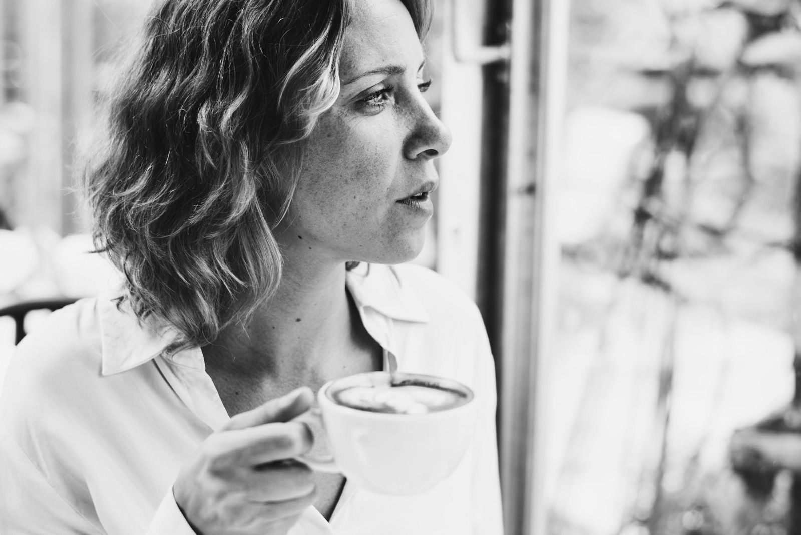A woman by a window holding a cup of coffee